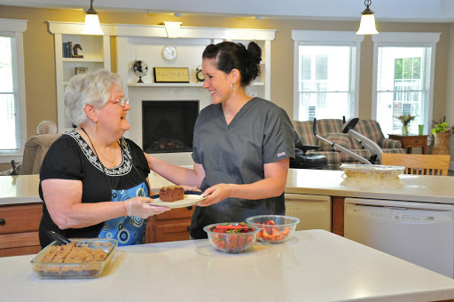 A caregiver serving food to an elderly woman in a warm kitchen setting.