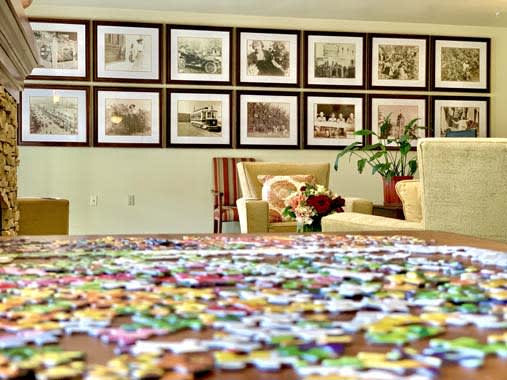 A cozy seating area with framed photos on the wall, a table covered in puzzle pieces, and a plant adding a touch of greenery.