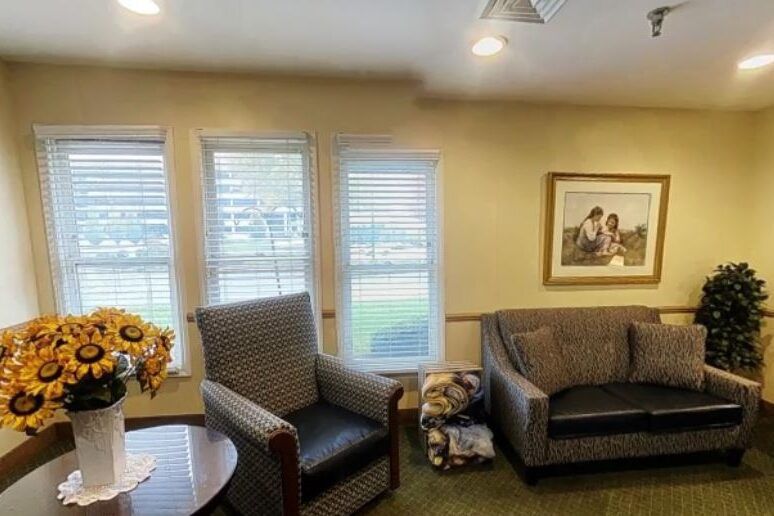 A cozy living room with comfortable chairs, multiple windows, and a framed painting on the wall.