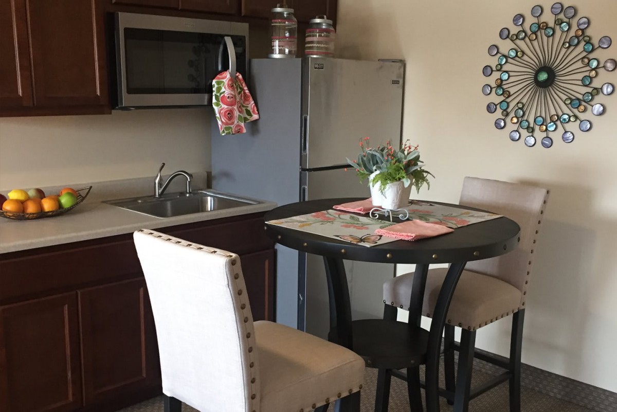 A cozy kitchen and dining area with a table and chairs, featuring a refrigerator, microwave, and decorative elements.