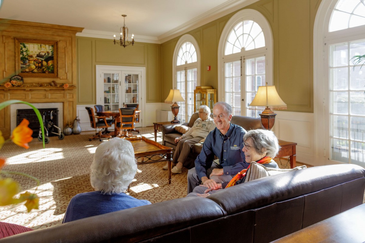 A group of seniors sitting together in a well-lit living room, engaged in conversation.