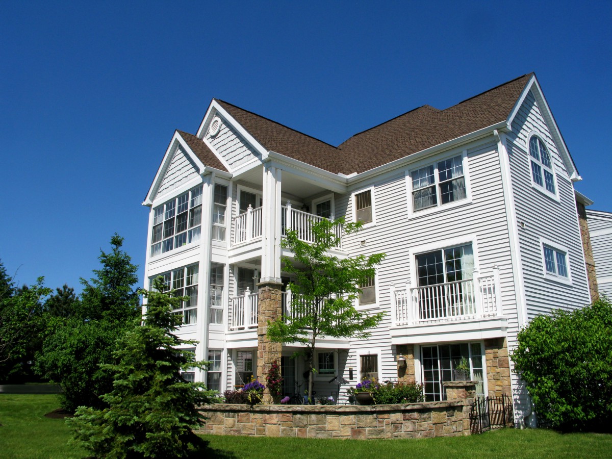 A modern residential apartment building with a well-maintained lawn and surrounding trees under a clear blue sky.