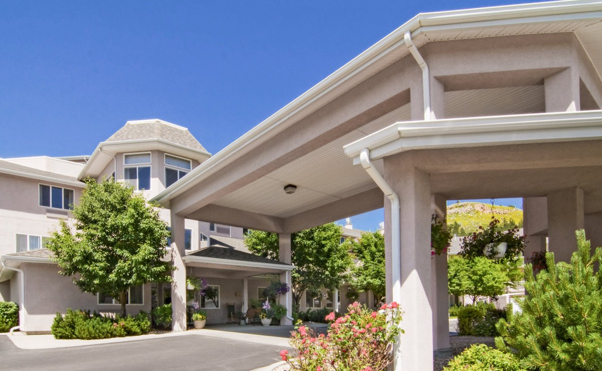 A view of a building entrance featuring columns and well-maintained landscaping under a clear blue sky.