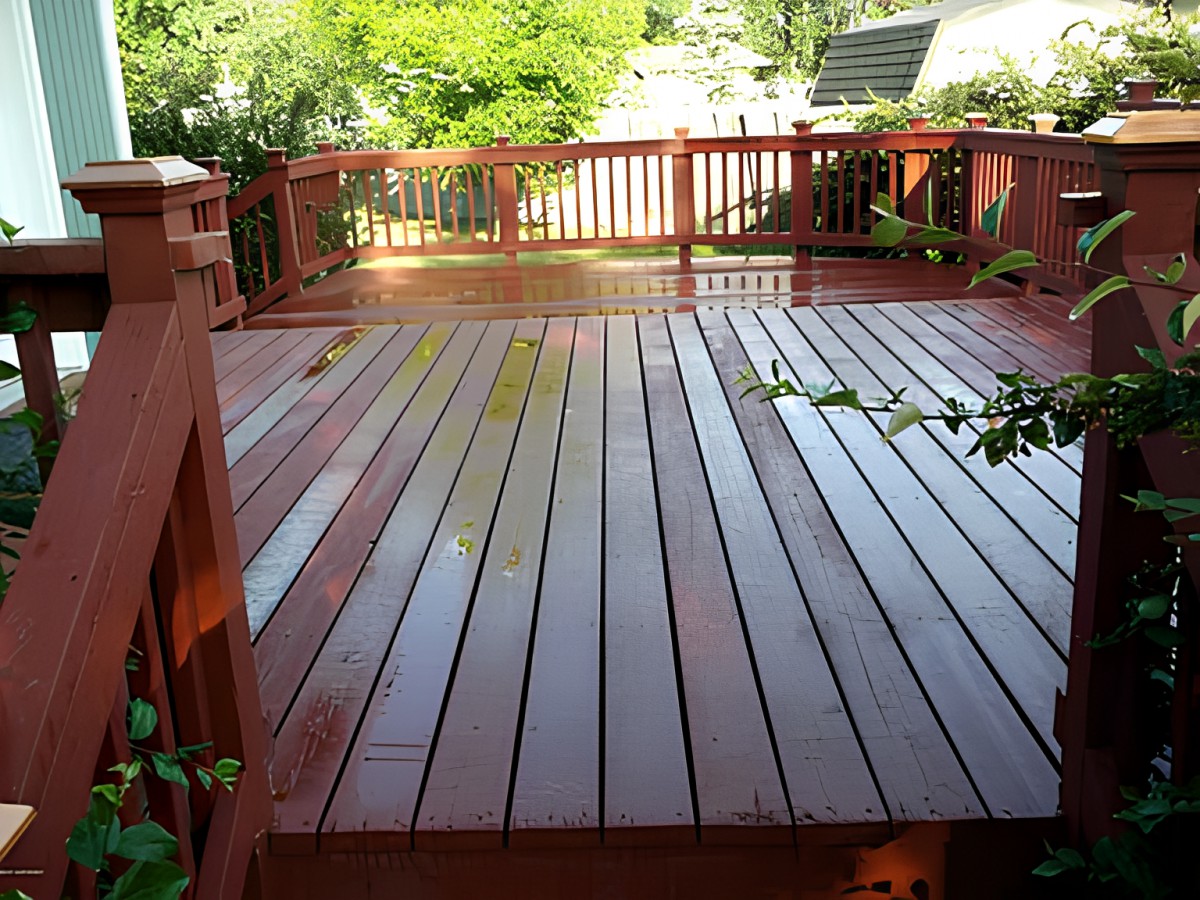 A wooden deck with sunlight reflecting on its surface, surrounded by a garden area.