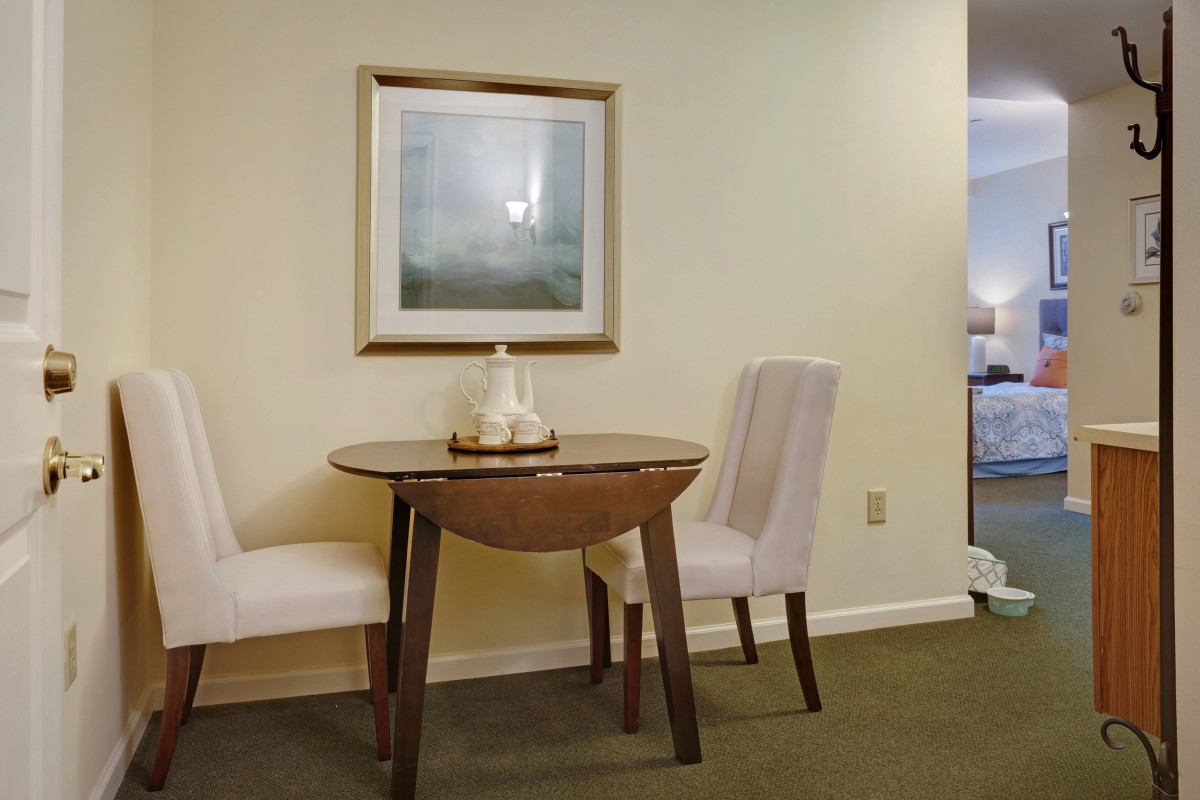 A cozy dining area featuring a wooden table with two upholstered chairs and framed artwork on the wall.