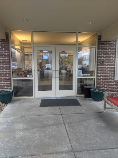 The entrance of a building featuring double doors and large windows, flanked by planters and a bench.