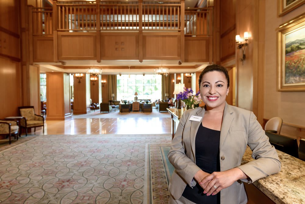 A woman stands smiling in a spacious hotel lobby.