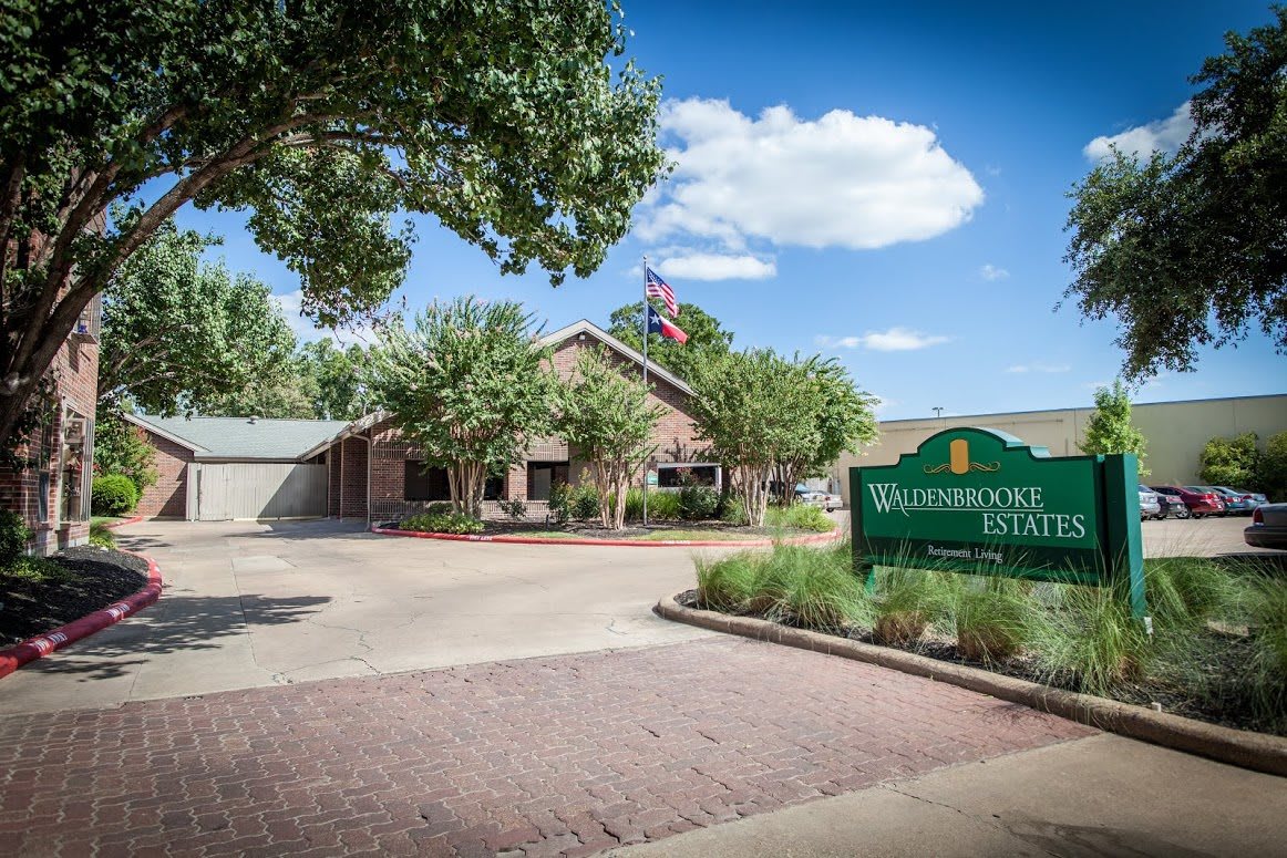 A serene view of a building with a welcoming sign, surrounded by trees and a clear blue sky.