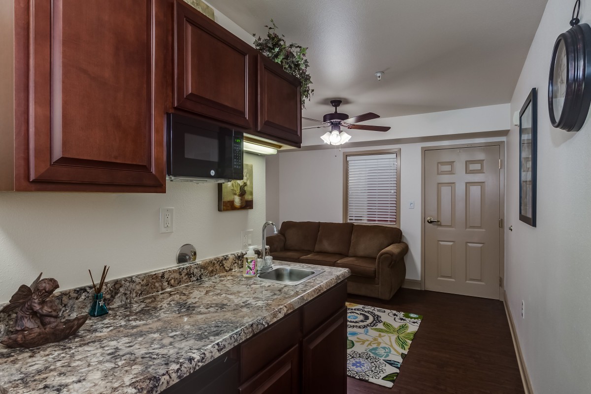 A cozy living space featuring a kitchen area with granite countertops, wooden cabinets, and a comfortable couch in an adjacent living room.