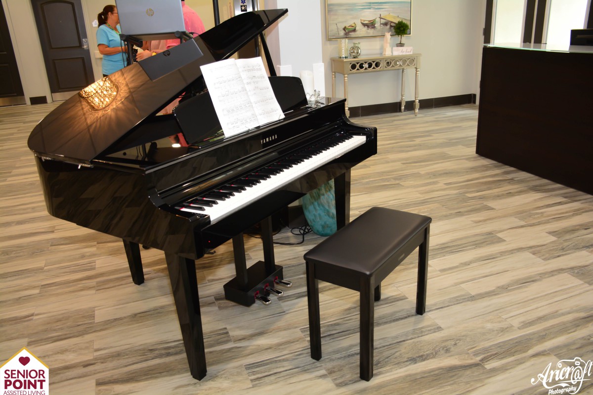 A black grand piano with a music sheet on the stand and a bench in front of it, set in an indoor space.