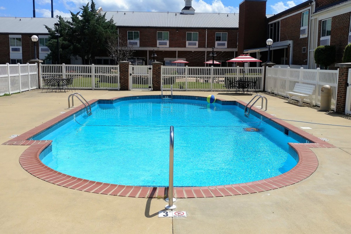 An outdoor swimming pool at a hotel with patio umbrellas and surrounding fence.