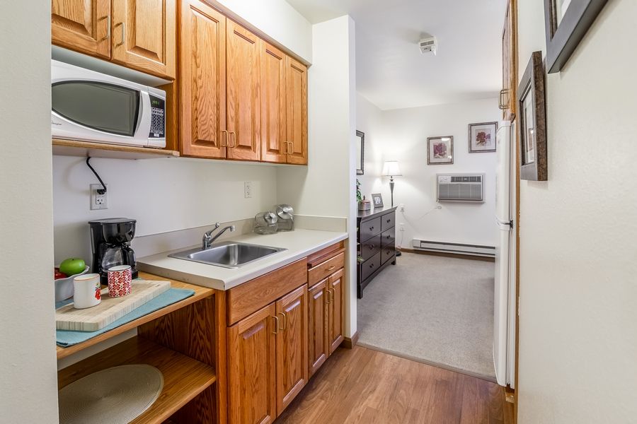 A compact kitchen area in an apartment with wooden cabinets, a sink, and a microwave.