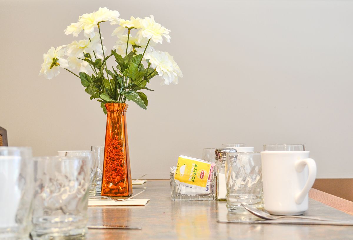 A table setting featuring a vase of daisies, glasses, sugar packets, and shakers.