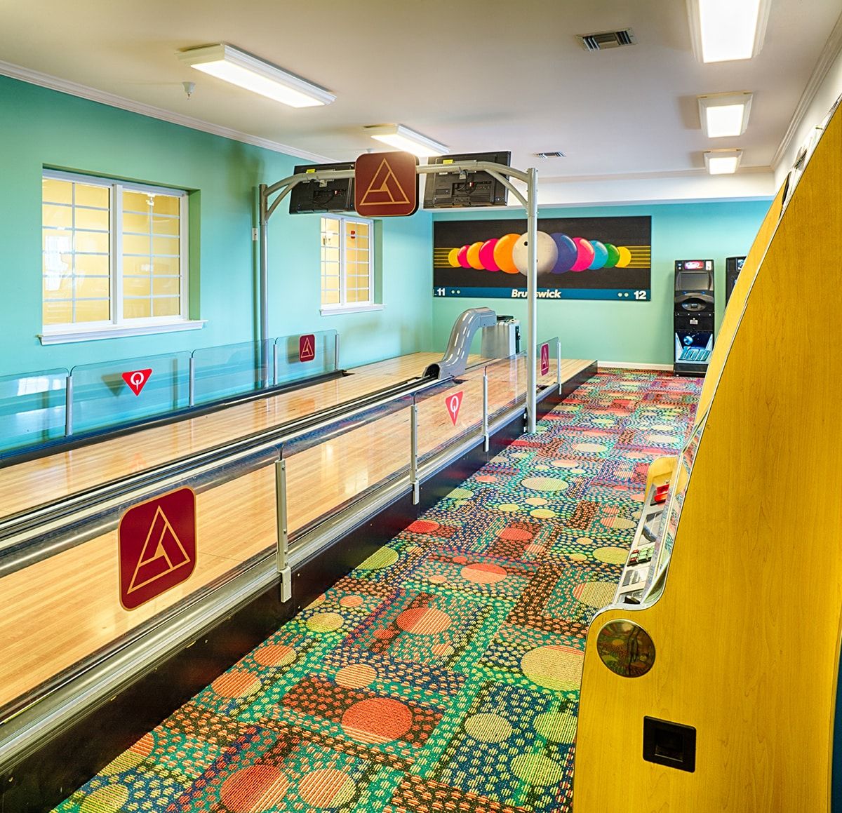 Brightly colored bowling alley with vibrant patterned carpet and two lanes.