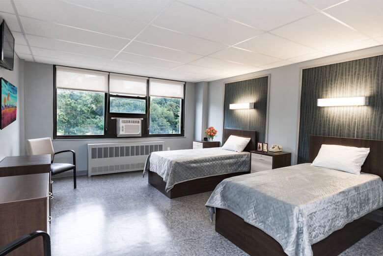 A modern bedroom with two neatly made beds, large windows, and natural light.