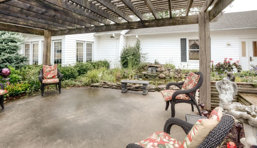 A cozy outdoor patio with seating under a pergola, surrounded by greenery.