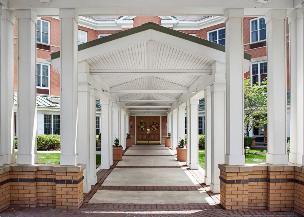 A covered walkway leading to the entrance of a building, featuring white columns and a brick facade.