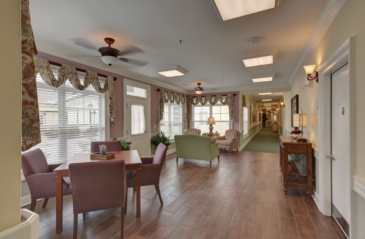 A cozy and well-lit interior space featuring a sitting and dining area with large windows, stylish decor, and a wooden floor.