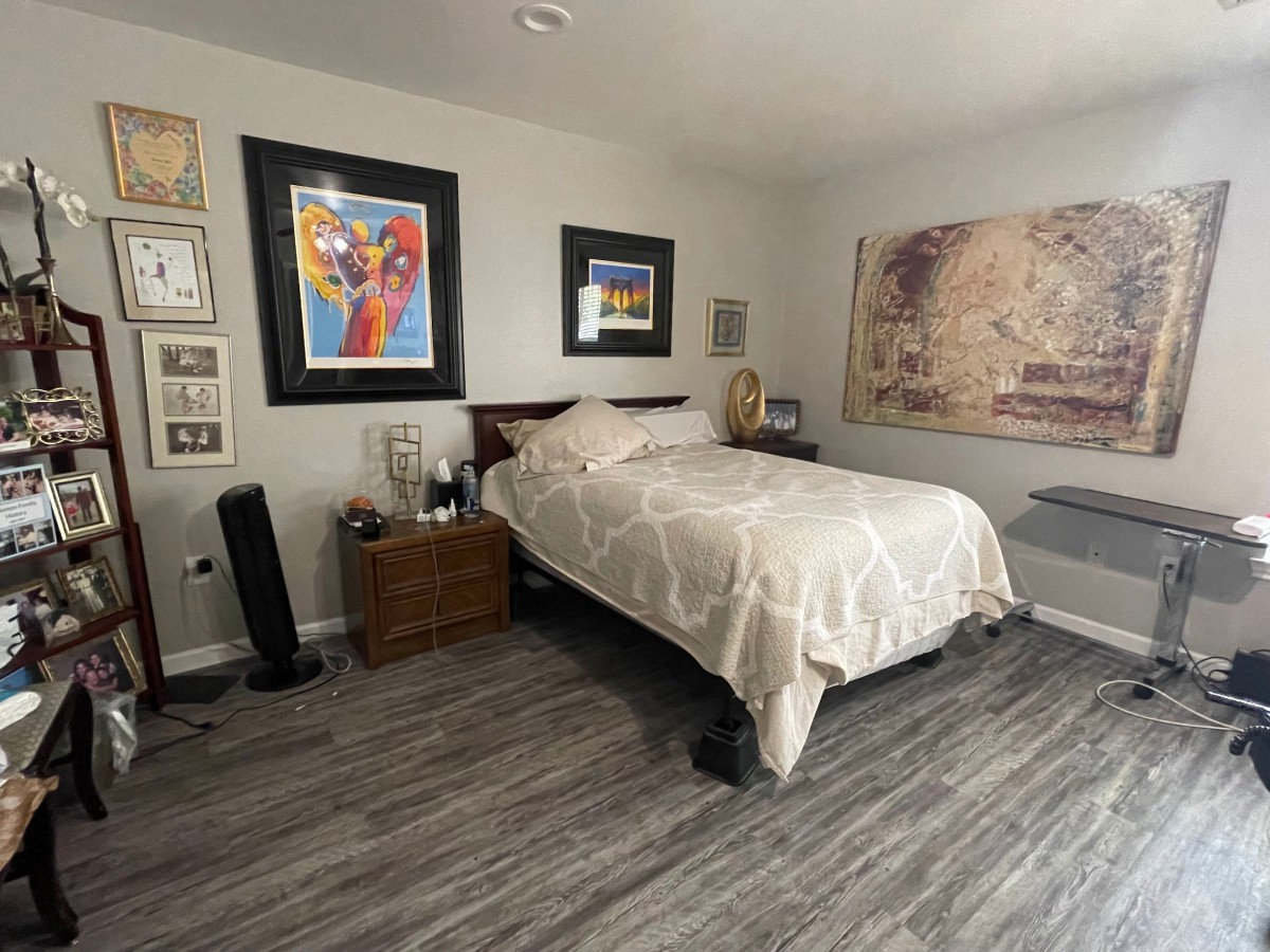 A modern bedroom featuring artwork on the walls, a neatly made bed, and sleek laminate flooring.