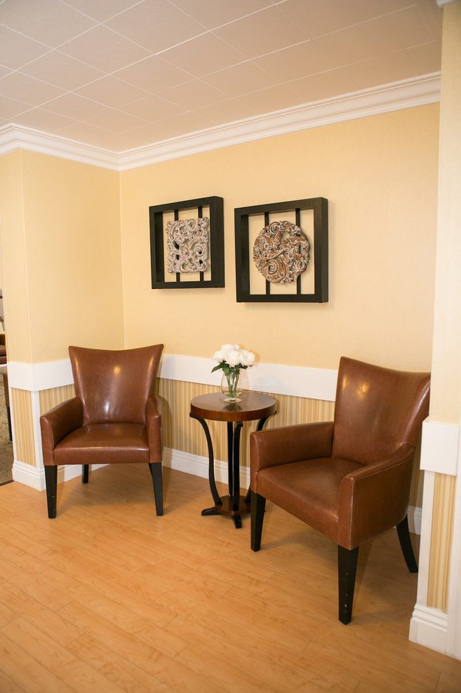 A cozy waiting area with two leather chairs, a small side table with flowers, and framed artwork on the wall.