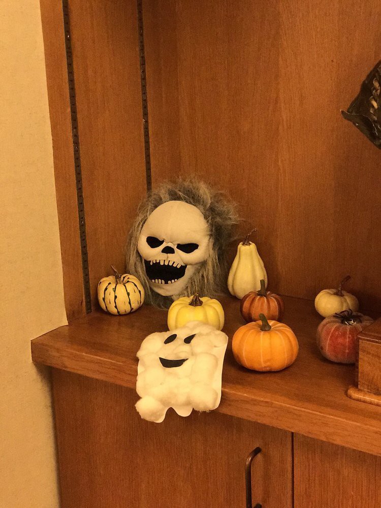 A Halloween-themed shelf display with a skull, ghost, and various pumpkins and gourds.