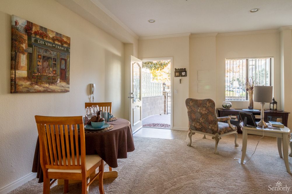 A cozy living room with a small dining area, featuring an open door and comfortable furniture.