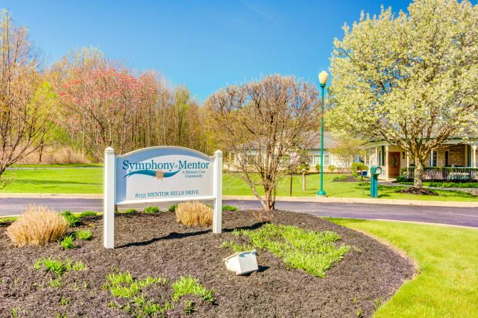A scenic park entrance with a welcoming sign and blossoming trees under a clear blue sky.