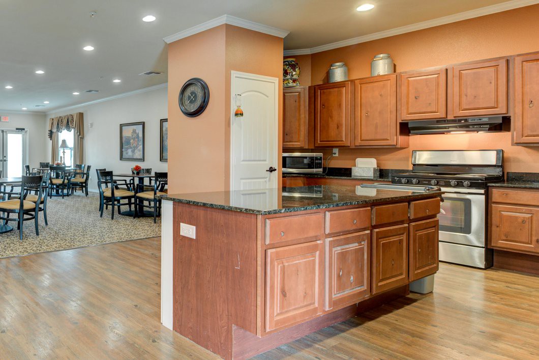 A modern kitchen with wooden cabinets and granite countertops, connected to an open dining area.