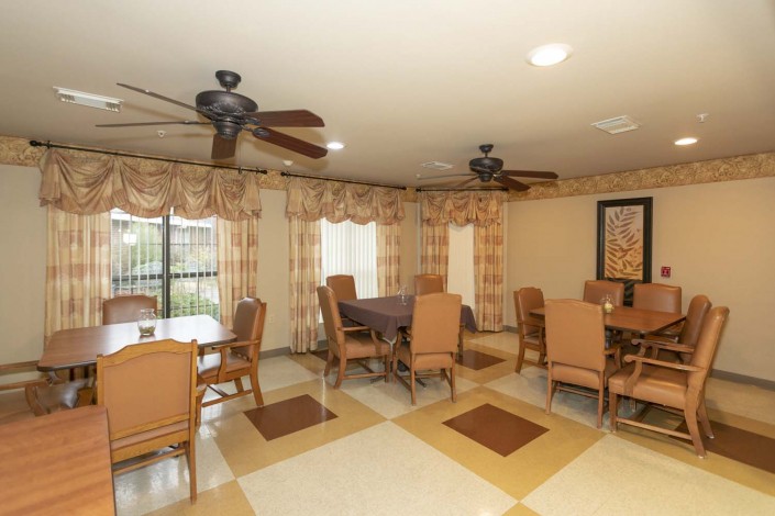 A well-lit dining room featuring multiple tables and chairs, ceiling fans, and decorative curtains.