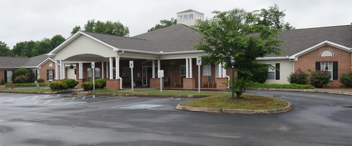 A small brick building with a covered entrance and an adjacent parking lot under an overcast sky.
