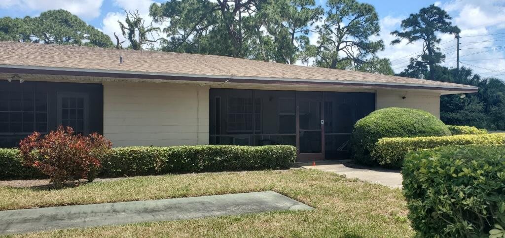 A small house with a screened porch surrounded by trees and shrubs.