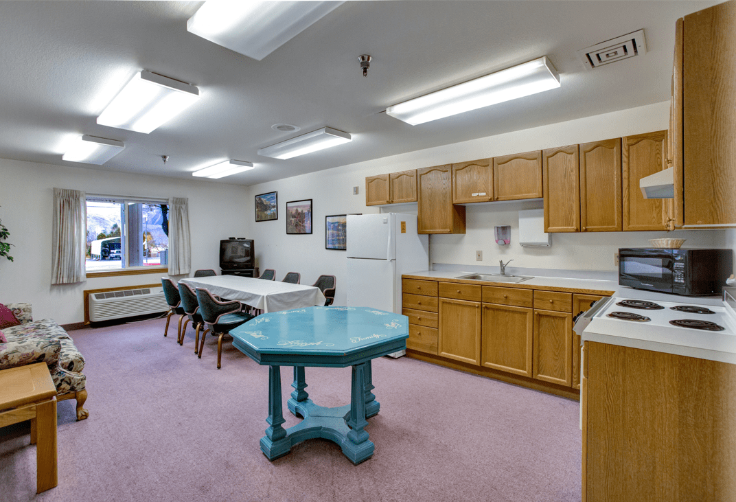 A well-lit communal kitchen and meeting area with a blue table and seating.