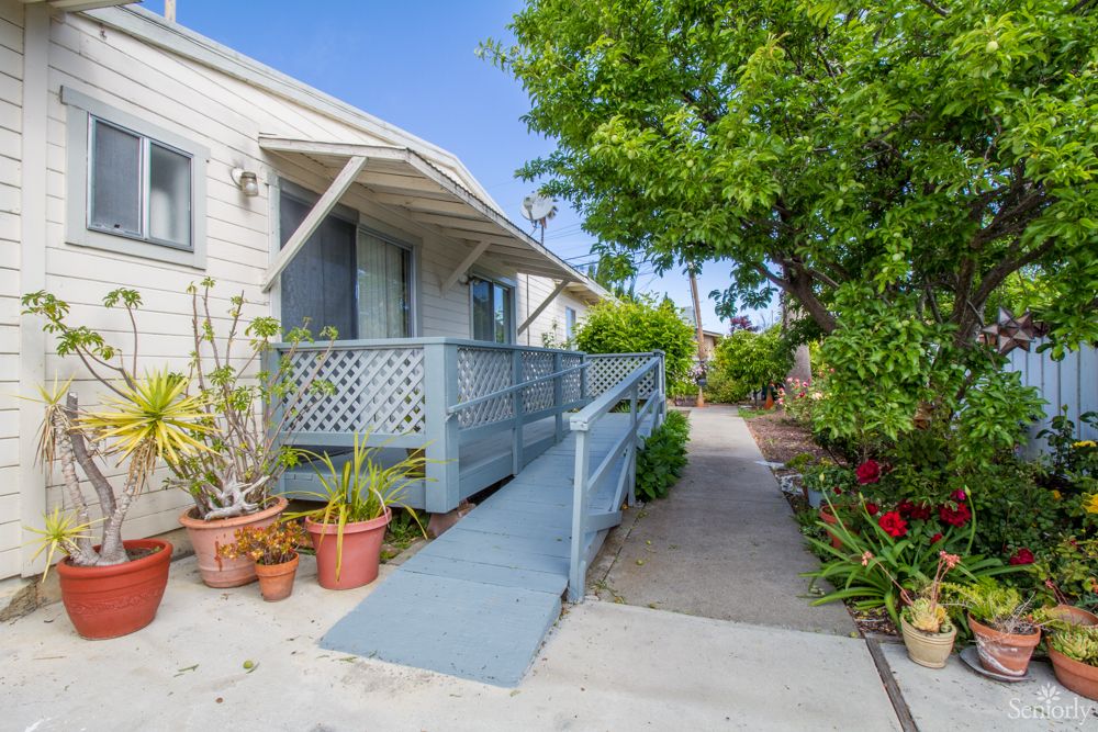A house with a wooden ramp leading to the entrance surrounded by a garden and potted plants.