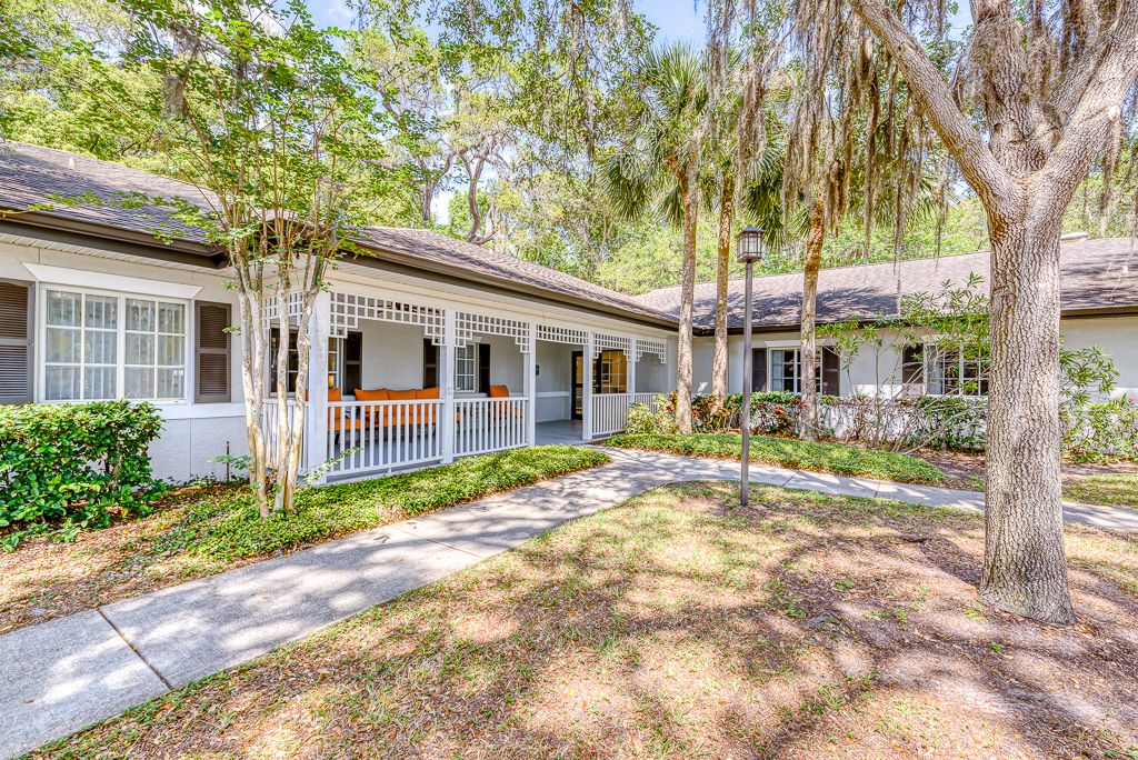 A charming house with a porch surrounded by trees and a garden walkway.