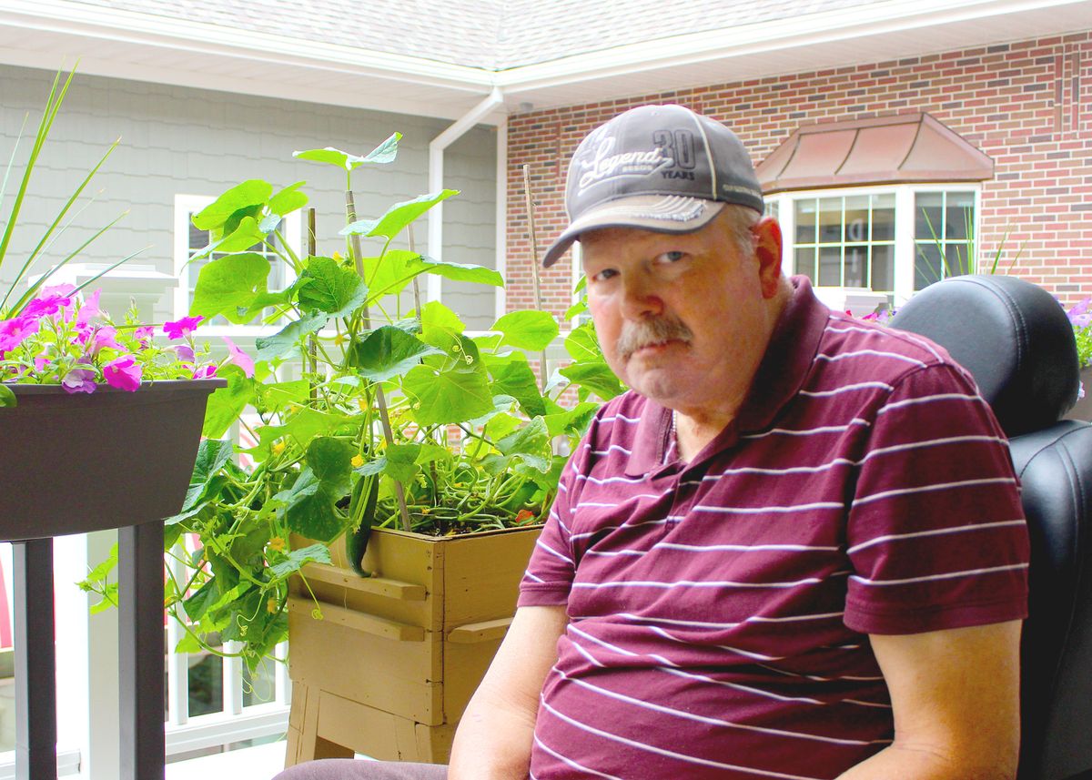 A man sitting on a porch with plants in the background.
