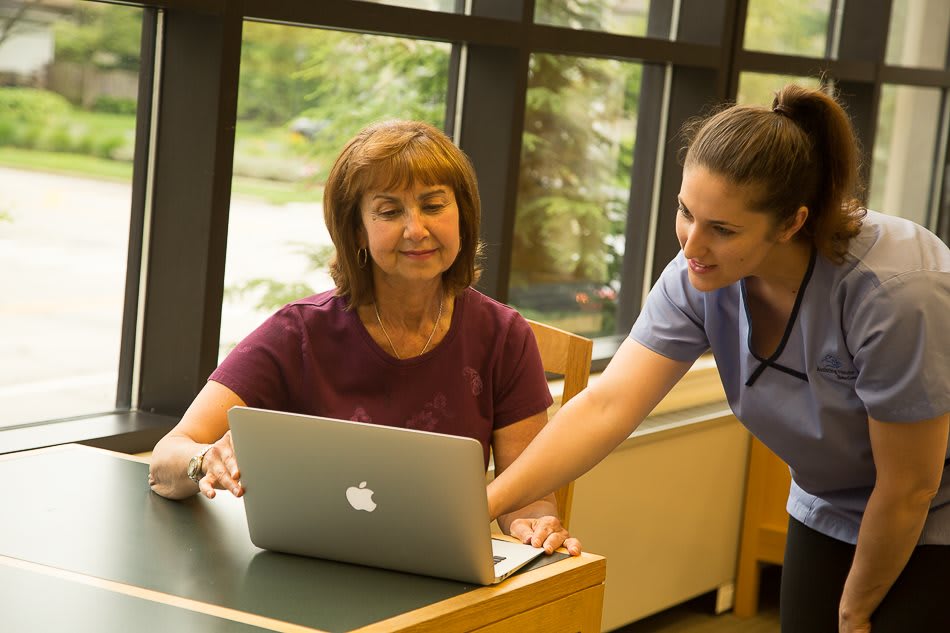 A woman is receiving guidance on using a laptop from another person in an indoor setting.