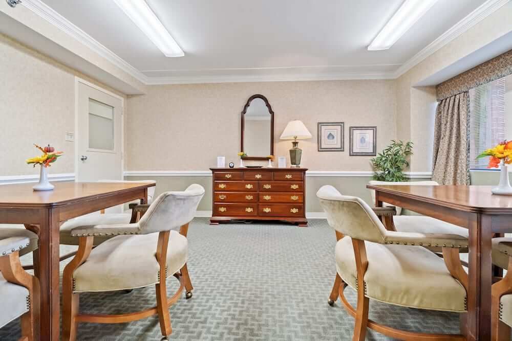 A meeting room with wooden furniture, including tables and cushioned chairs, adorned with a lamp, mirror, and decorative elements.