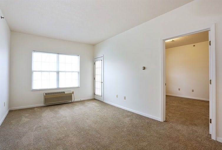 An empty room with carpeted flooring, white walls, and a large window.