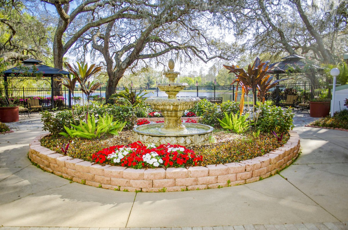 A beautifully landscaped garden with a central fountain, surrounded by vibrant flowers and lush trees.
