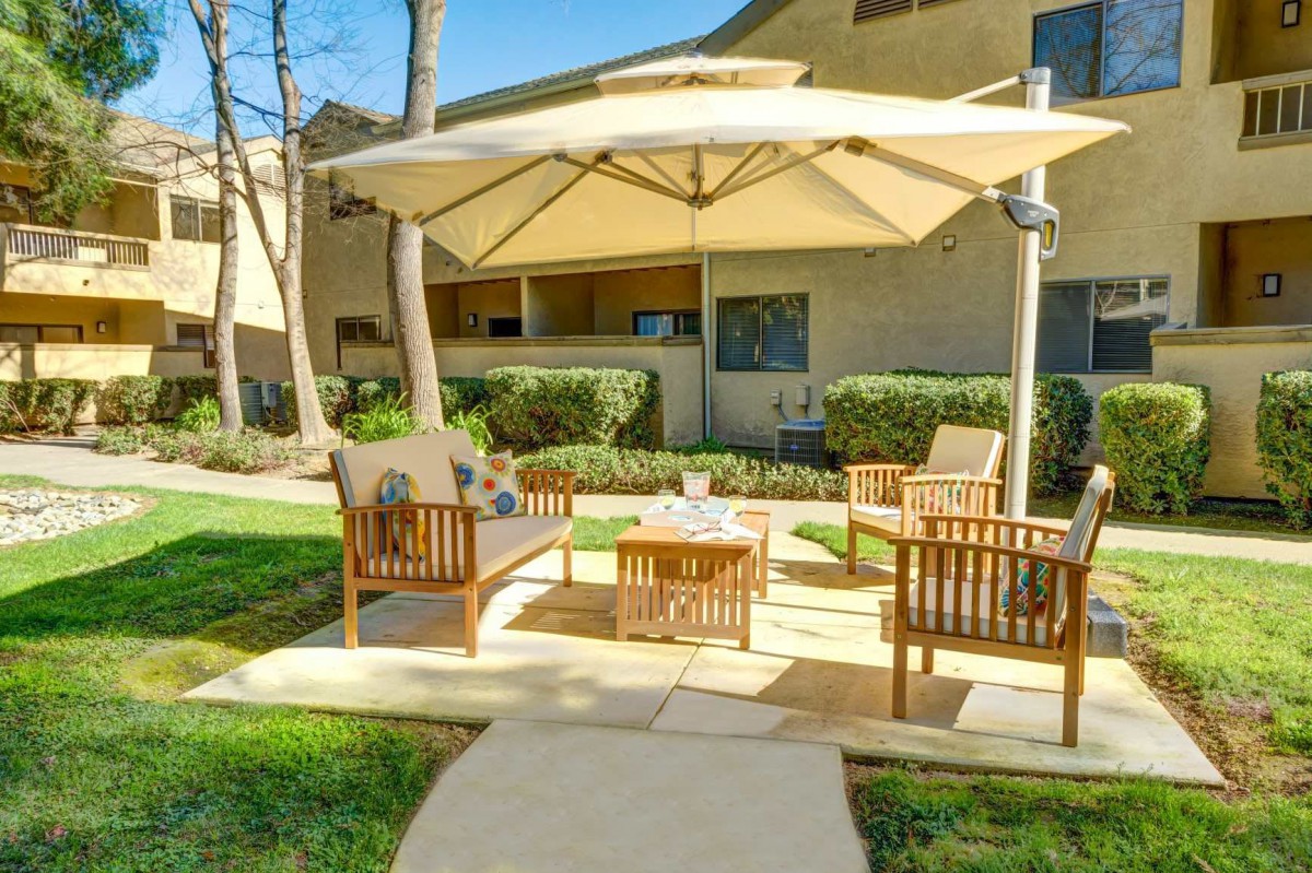A cozy outdoor seating area featuring wooden chairs and a table under a large umbrella, set in a well-maintained garden.