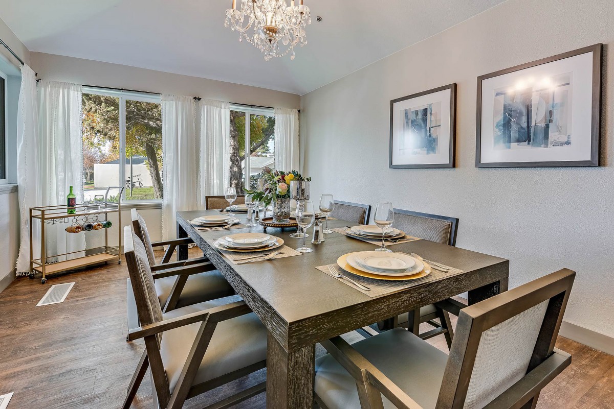 A modern dining room with a wooden table set for a meal, illuminated by a chandelier and featuring minimalist decor and artwork.