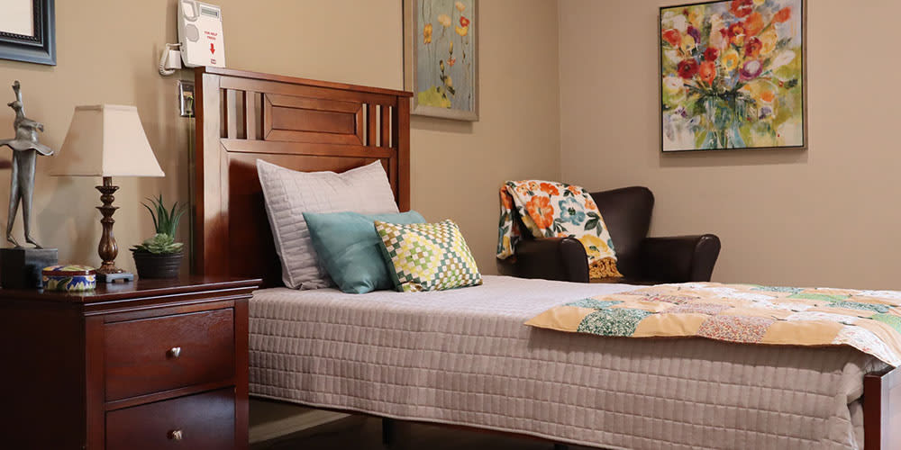 A cozy bedroom with a neatly made bed, decorative pillows, and a comfortable chair adorned with a colorful throw.