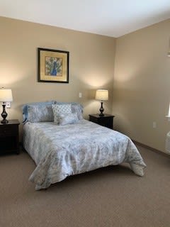 A neatly arranged bedroom featuring a bed with patterned bedding, two bedside lamps, and wall artwork.