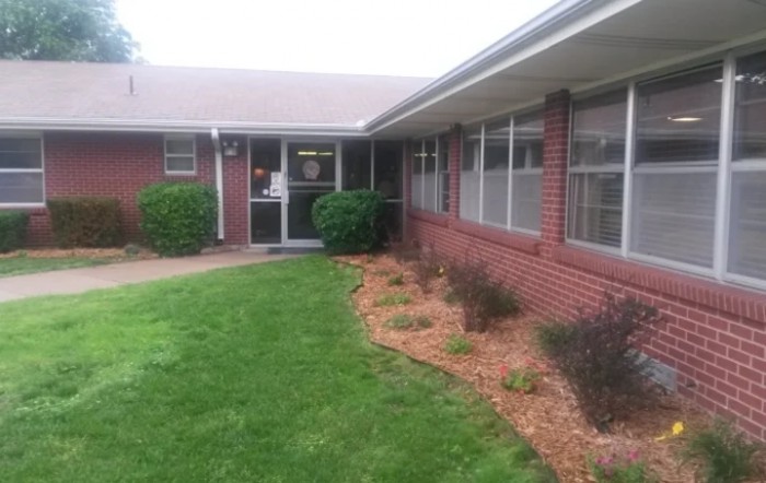 A brick building with a well-maintained lawn and shrubbery leading to an entrance.