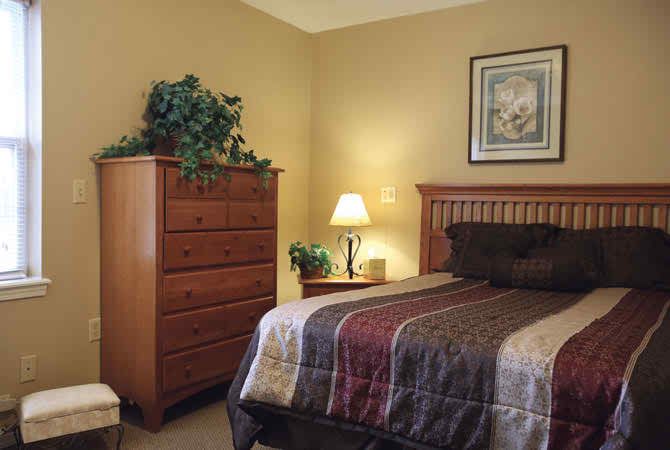 A cozy bedroom with a wooden bed, dresser, and lamp, decorated in warm tones.