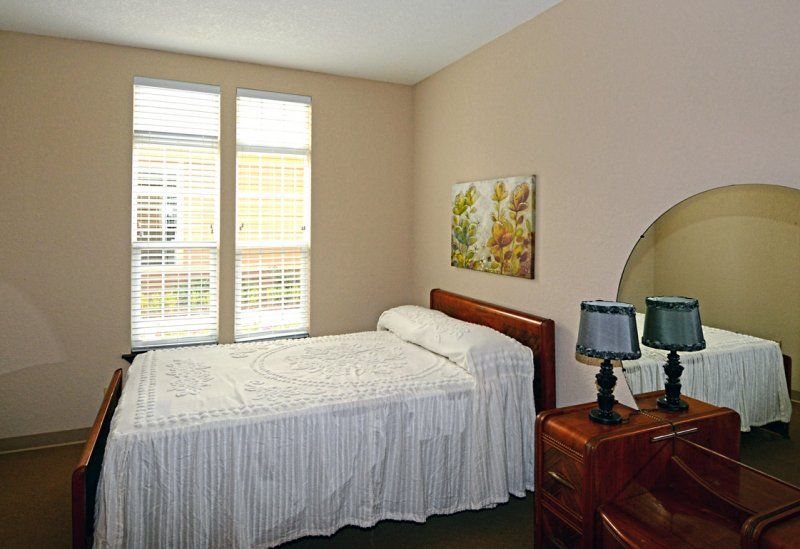 A cozy bedroom with a single bed, bedside table, and large windows.
