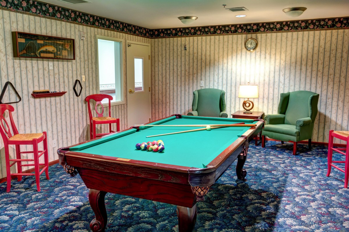A cozy game room featuring a billiards table with a cue and balls set up, surrounded by comfortable seating and elegant decor.