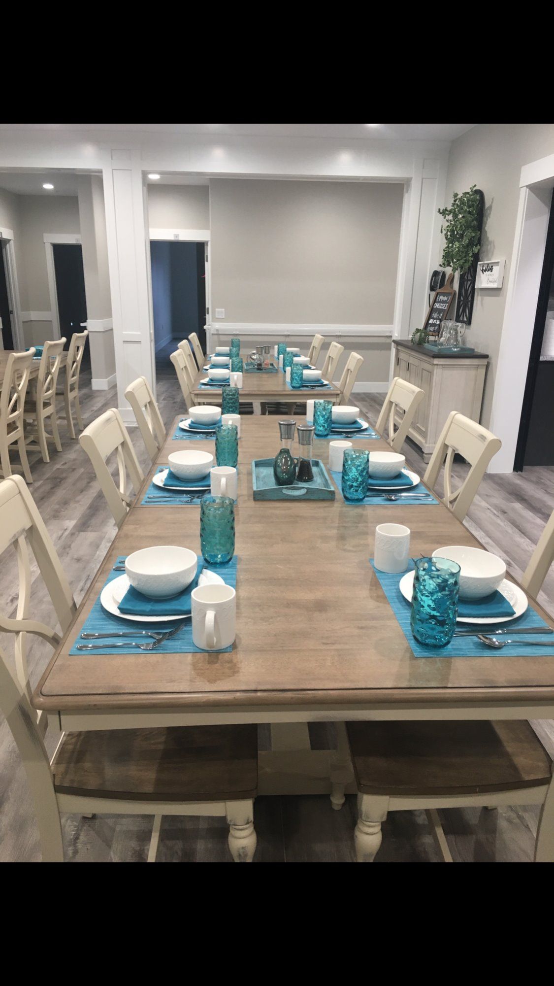 A neatly arranged dining room with a long wooden table, white chairs, and blue accented place settings.