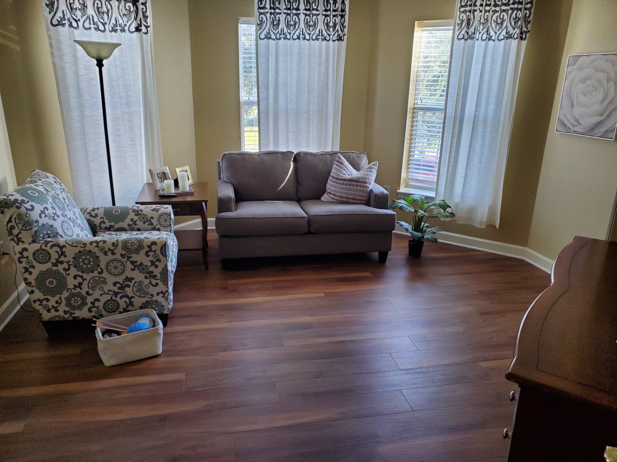 A cozy living room with a sofa, armchair, and large windows with curtains.