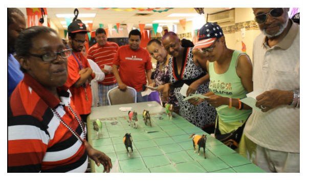 A group of people gathered around a table playing a miniature horse racing game indoors.